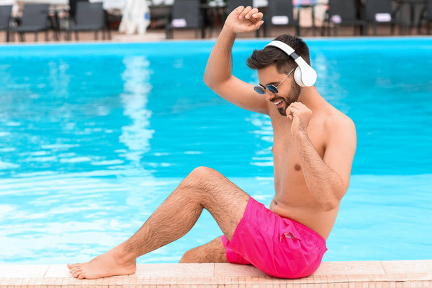 Młody człowiek słuchający muzyki przy basenie - Zdjęcie, obraz