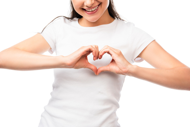 καλλιεργημένη άποψη της νεαρής γυναίκας που δείχνει το σημάδι της καρδιάς με τα χέρια απομονώνονται σε λευκό - Φωτογραφία, εικόνα