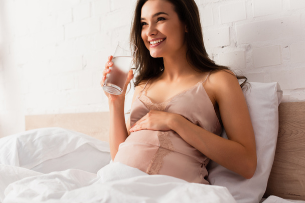 young pregnant woman holding glass of water and touching belly  - Foto, immagini