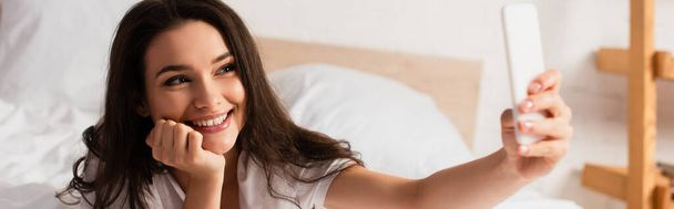 plano panorámico de la joven mujer tomando selfie en el dormitorio  - Foto, Imagen