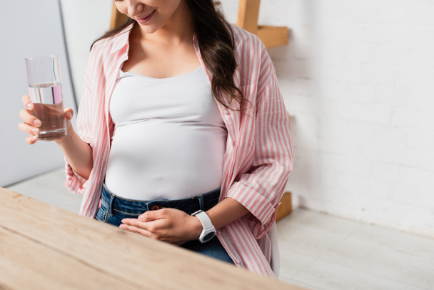 cropped view of pregnant woman touching belly and holding glass of water  - Photo, Image