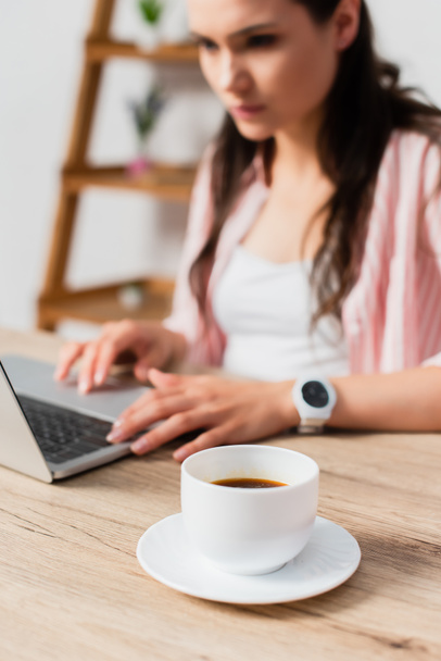 selectieve focus van kopje met koffie in de buurt van freelancer met behulp van laptop  - Foto, afbeelding