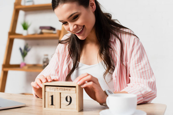 selective focus of brunette woman touching wooden cubes with date near cup  - Fotó, kép