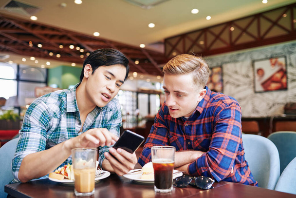 Jeune homme asiatique déjeuner avec un ami dans un café et montrant une nouvelle application mobile sur smartphone à un ami - Photo, image