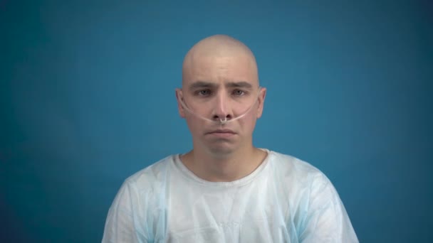 Egy kopasz fiatalember onkológiával szomorúan néz a kamerába kék háttérrel. Kemoterápia miatti hajhullás. - Felvétel, videó