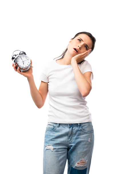 tired brunette woman in white t-shirt and jeans holding retro alarm clock isolated on white - Photo, Image