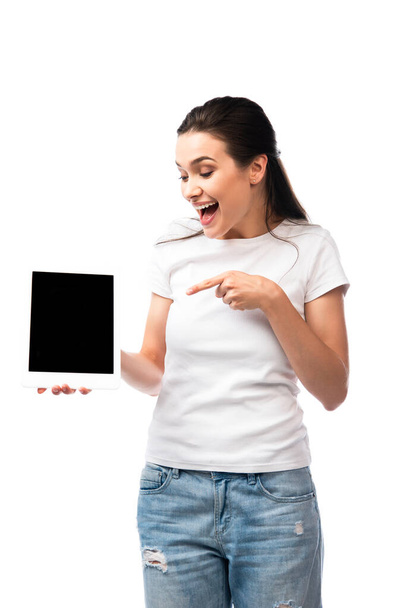 mujer morena en camiseta blanca apuntando con el dedo a la tableta digital con pantalla en blanco aislado en blanco  - Foto, imagen