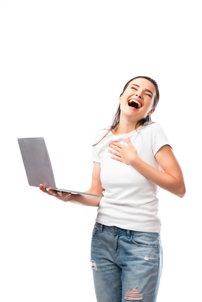 brunetka kobieta w biały t-shirt śmieje się i trzyma laptop odizolowany na biały  - Zdjęcie, obraz