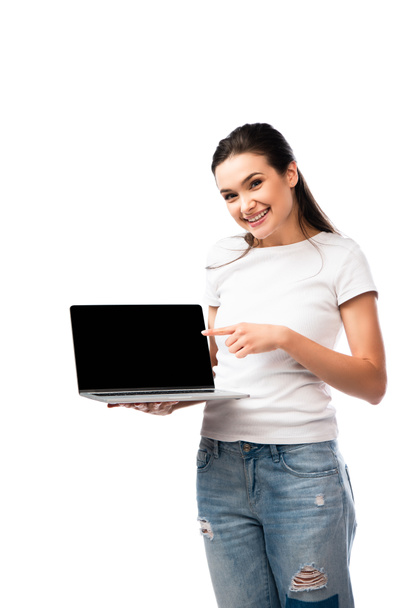 brunette woman in white t-shirt pointing with finger at laptop with blank screen isolated on white  - Φωτογραφία, εικόνα