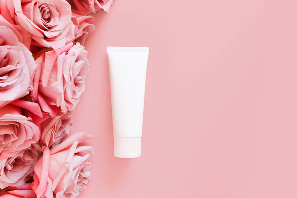 Top view of mockup of white squeeze bottle plastic tube and pink roses on a pastel pink background. Bottle for branding and label. Natural organic spa cosmetic. Copy space, Flower flatlay. - Photo, Image