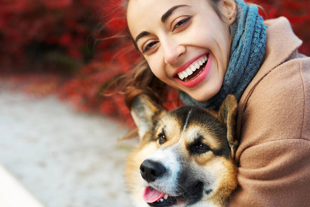 close-up autumn portrait happy woman and pet Welsh Corgi dog with funny face on red fall leaves background. - Photo, image