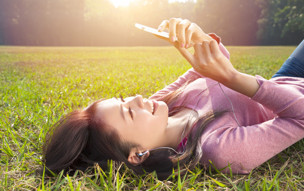 smiling young woman touching cell phone and lying on meadow - Photo, Image
