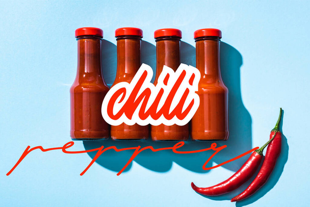 Top view of chill pepper lettering near tomato sauce in bottles on blue background - Foto, Imagem