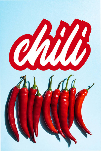 Top view of fresh and organic peppers near chili lettering on blue  - Foto, imagen