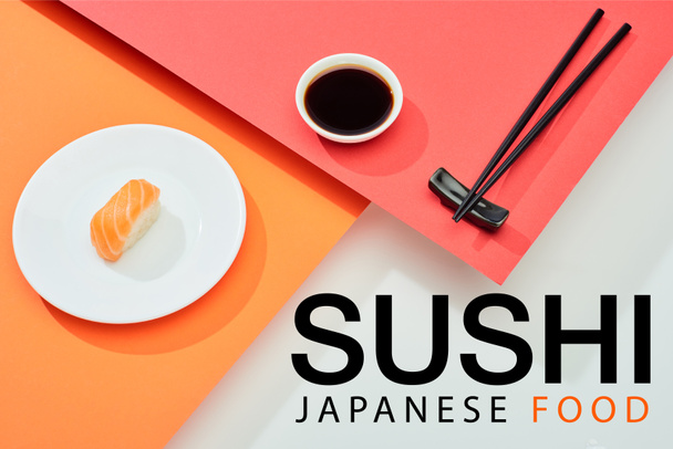 frische Nigiri mit Lachs in der Nähe von Sojasauce, Essstäbchen und japanischen Sushi-Schriftzug auf roter, orangefarbener und weißer Oberfläche - Foto, Bild