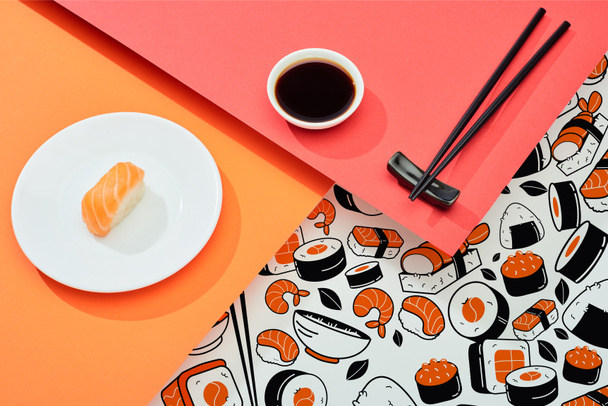 tuore nigiri lohen kanssa lähellä soijakastiketta, syömäpuikkoja ja sushi-kuvitus punaisella, oranssilla, valkoisella pinnalla - Valokuva, kuva
