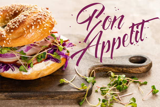 fresh and delicious bagel near bon appetit lettering on wooden cutting board - Fotó, kép
