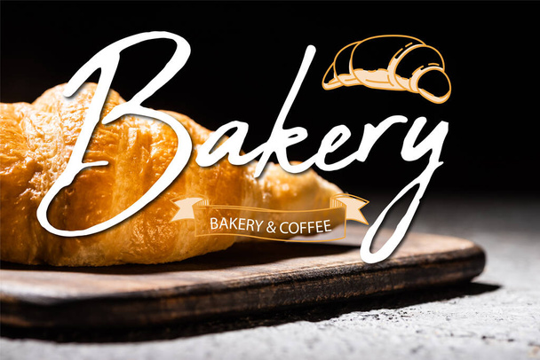 close-up van gebakken croissant op houten snijplank bij bakkerij en koffiebelettering op zwart - Foto, afbeelding