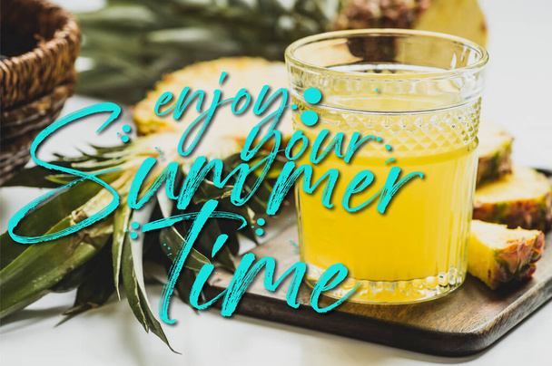 selective focus of pineapple juice in glass near delicious fruit on cutting board and enjoy your summer time lettering on white  - Fotó, kép
