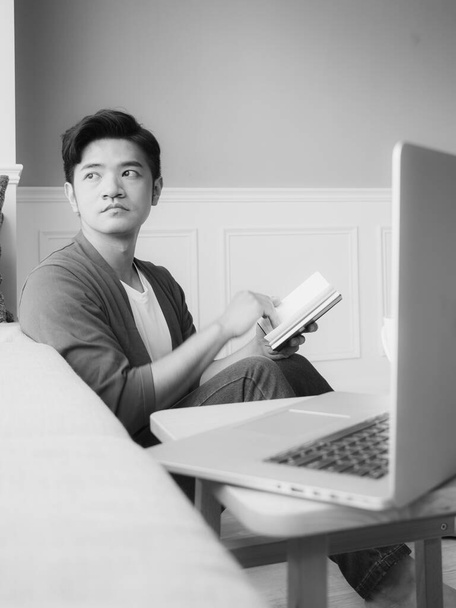 Young asian man reading a book while relaxing at home in black and white - Foto, immagini