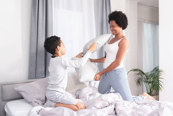 Playful mother and son fighting with pillow on bed - Foto, Imagen