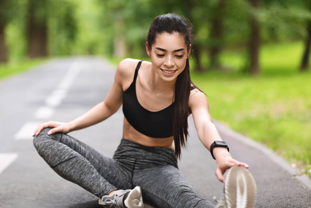 Fiatal fitness kocogó lány nyújtózkodó lábak előtt fut a parkban, edzés szabadban - Fotó, kép