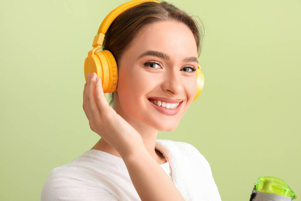 Sporty young woman with headphones and water on color background - Fotoğraf, Görsel