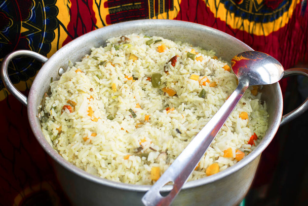 Uma panela de arroz frito nigeriano decorado com feijão verde, cenouras e pimenta fatiada, cozido e pronto para ser servido com uma colher no lado - Foto, Imagem
