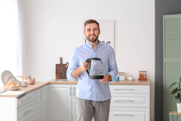 Young man with electric kettle at home - Photo, Image