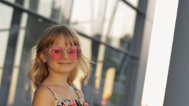 Miúda ao pôr do sol a usar óculos de sol no aeroporto. Criança turística. Olhar estilo havaiano. Férias
 - Foto, Imagem