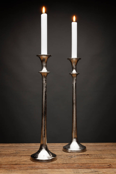 2 pitkä hopea kynttilän pidikkeet ja hehkuva kynttilät, ammuttiin puinen pöytä, tummanharmaa tausta - Valokuva, kuva