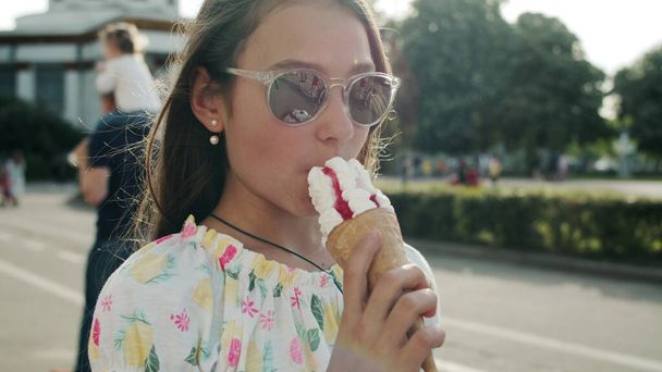 可愛い娘がアイスクリームコーンを食べてる。リラックスしたティーン女の子ウォーキングで遊園地 - 写真・画像