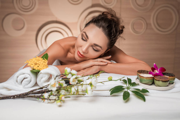 Femme heureuse allongée sur la table avec des fleurs, serviette après les procédures de spa - Photo, image