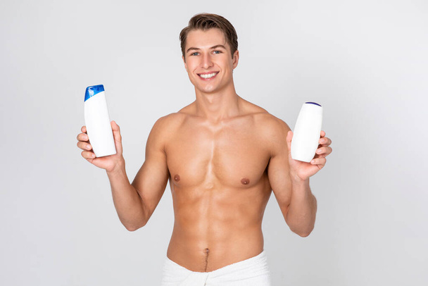 Handsome smiling guy standing with shampoo in hands - 写真・画像