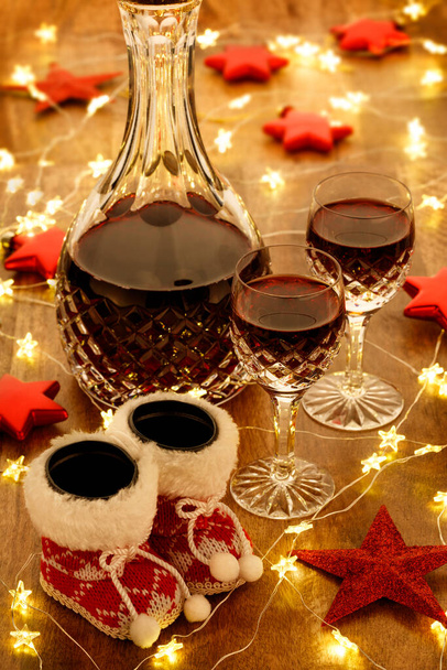 Μια καράφα από πορτό και κρυστάλλινα ποτήρια με χριστουγεννιάτικα φώτα, μπιχλιμπίδια και διακοσμητικά κόκκινα αστέρια, σε ξύλινο τραπέζι - Φωτογραφία, εικόνα