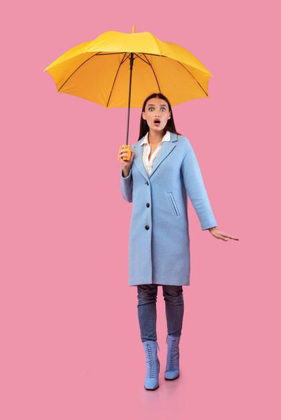 Portrait of shocked girl holding yellow umbrella - Photo, Image
