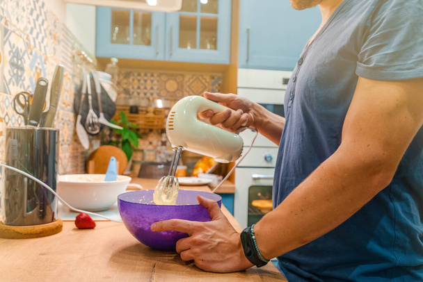 Un joven en una cocina luminosa casa amasa la masa para una magdalena con una batidora - Foto, imagen