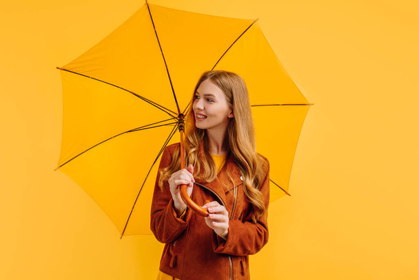 happy girl, in a bright yellow dress and an autumn jacket, stands with a yellow umbrella on a yellow background - Photo, image