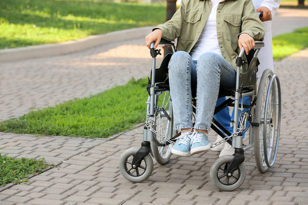 Doctor and young woman in wheelchair outdoors - Photo, Image
