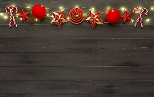 Een reeks rode kerstversieringen, lampjes en snoepstokjes, op een gedestabiliseerde donkere houten achtergrond - Foto, afbeelding