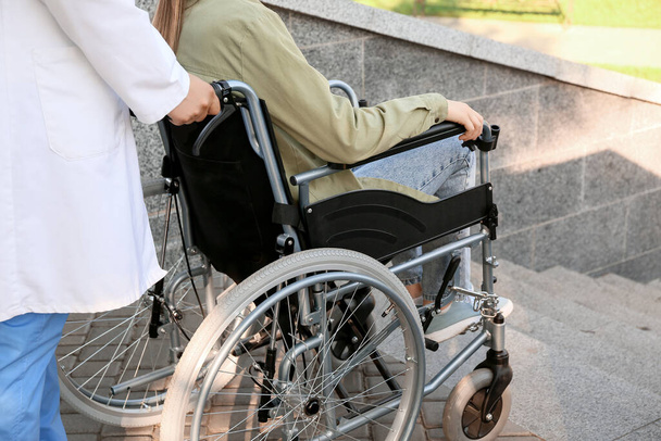 Doutor e jovem em cadeira de rodas perto de escadas ao ar livre
 - Foto, Imagem