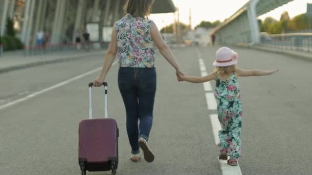 Äiti ja tytär kävelevät ulos lentokentälle. Nainen kantaa matkalaukkua. Lapsen ja äidin loma - Materiaali, video