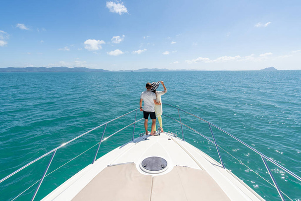 Back view of a sweet couple standing on edge of luxury yacht. Brunette wearing straw hat and fashion summer suit and sunglasses. Luxury seascape - Foto, imagen