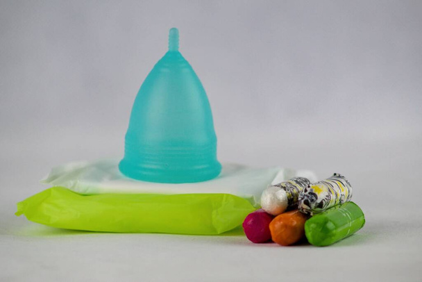 Blaue Menstruationstasse und Sanitärservietten und Tampons isoliert auf weißem Hintergrund. Menstruationstasse - ein modernes Hilfsmittel während der Menstruation für eine moderne Frau im Vergleich zu Sanitärservietten und Tampons. - Foto, Bild