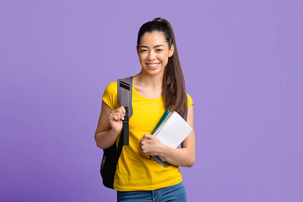 Bildungskonzept. Asiatische Studentin mit Arbeitsbüchern und Rucksack lächelt in die Kamera - Foto, Bild