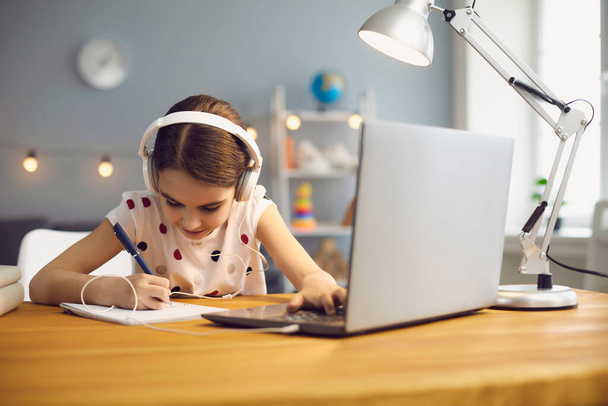 Online education for children. A girl in headphones makes an online lesson using a computer video call to a virtual teacher at home. - Φωτογραφία, εικόνα