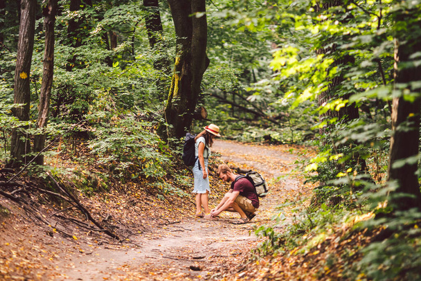 Hipster pareja excursionista se detiene para atar su zapato en el sendero de verano en el bosque. Hombre atando zapatos de mujer. Estilo de vida activo divertido al aire libre. Los campistas atando cordones de zapatos preparándose para la caminata. Cuidado, amor en el viaje. - Foto, Imagen