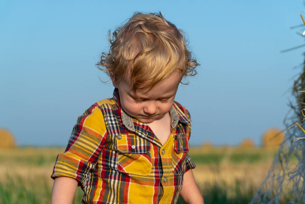 Little fair-haired boy playing on a wheat field with bales - Фото, изображение