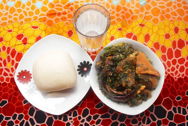 Pohled shora na servírovanou mísu s bramborovou kaší a hustou zeleninovou polévkou vařenou ze sušených ryb, kpomo, shaki a raků. Tohle je tradiční nigerijské jídlo. - Fotografie, Obrázek