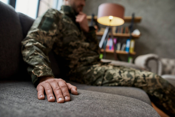 Close up of hand of military man in camouflage sitting on the couch during therapy session. Soldier suffering from depression, psychological trauma. PTSD concept - Valokuva, kuva